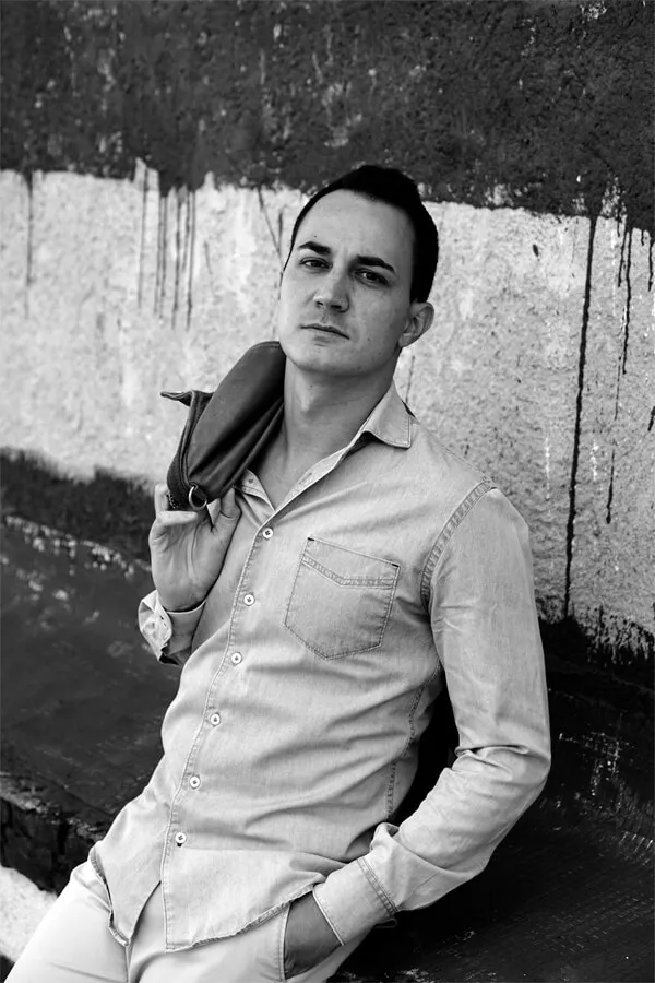 Apoyado en una pared desconchada, camisa clara, en blanco y negro