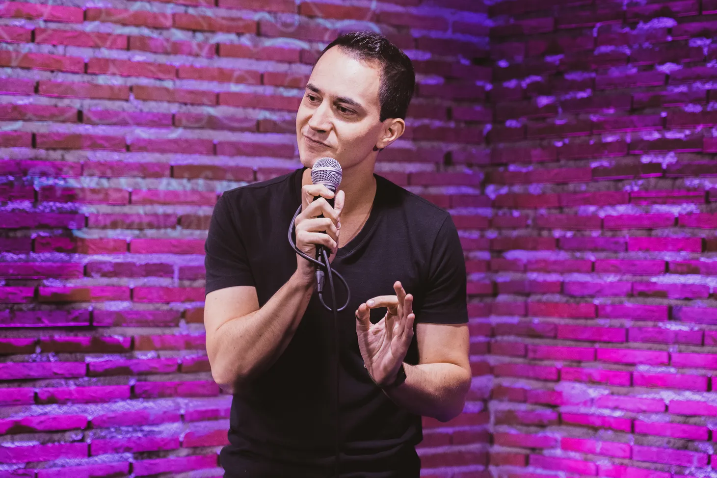 Pablo Alcaraz con un micrófono en el escenario, ante una pared de ladrillo iluminada en violeta